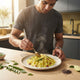 A young South Asian man preparing a bowl of fluffy Poha in a sunlit kitchen.